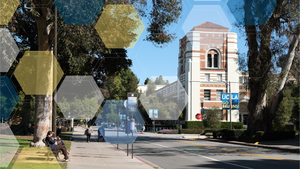 Blue UCLA Go Bruins! sign in front of a white and brick building. Trees on the right and left sides. 
